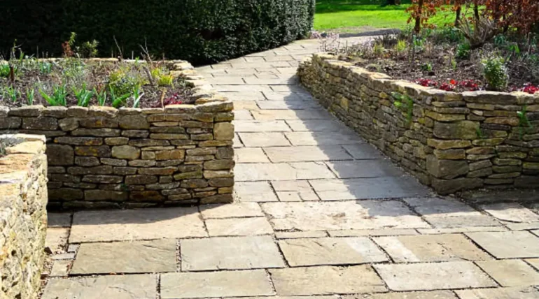 A hardscaping design with a stone walkway, stacked stone retaining walls, and raised garden beds in a landscaped yard.