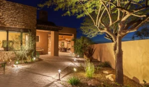 Warm landscape lighting installation along stone walkway highlighting trees, walls, and entrance of Austin home at night.