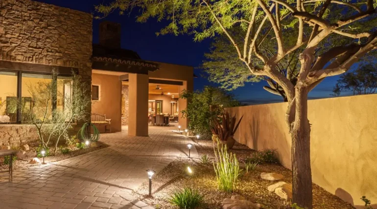 Warm landscape lighting installation along stone walkway highlighting trees, walls, and entrance of Austin home at night.