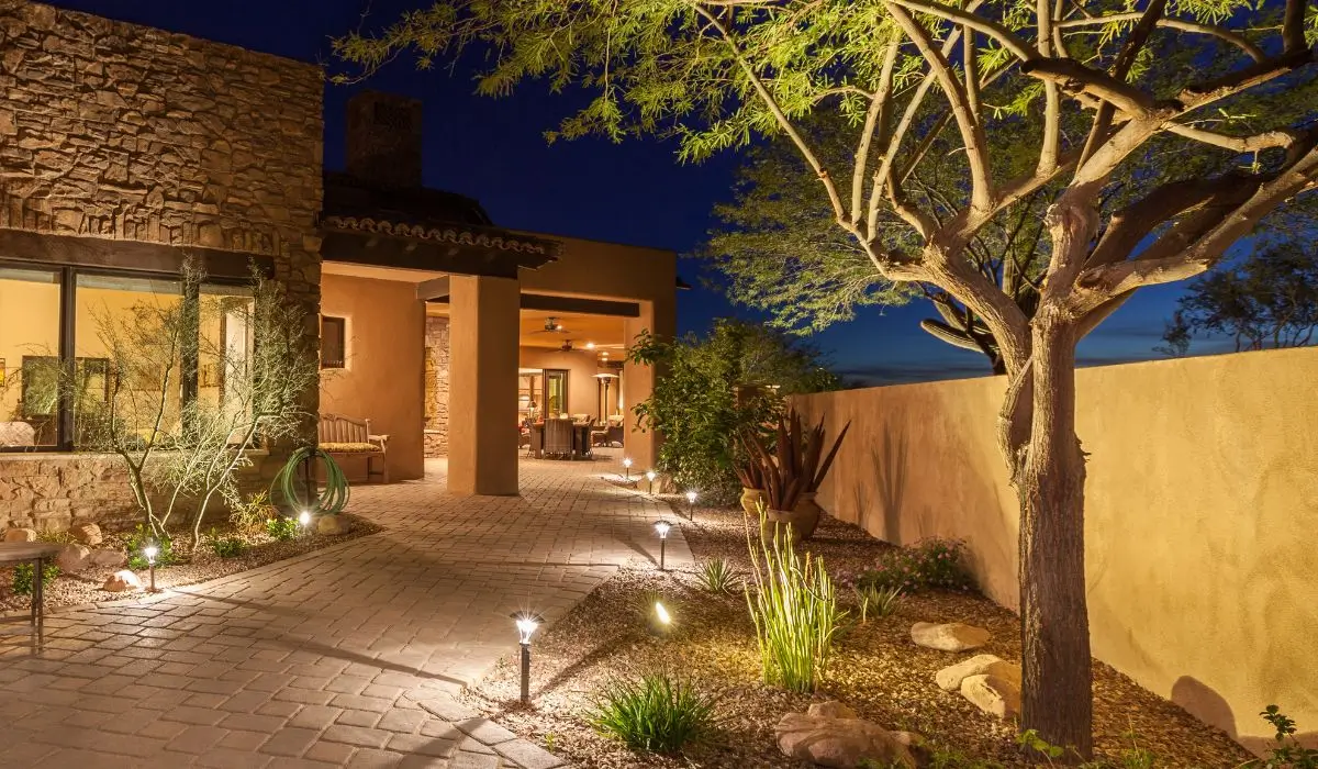Warm landscape lighting installation along stone walkway highlighting trees, walls, and entrance of Austin home at night.