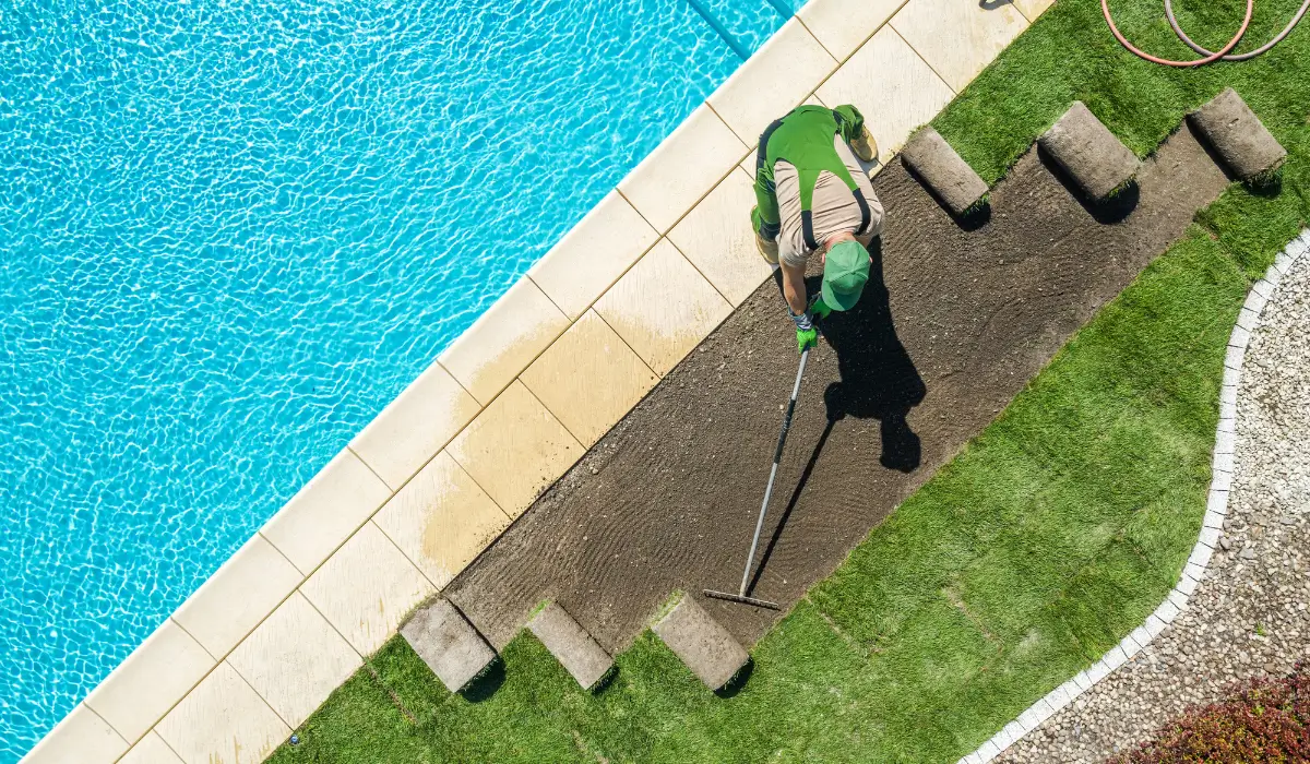Professional landscaper leveling soil to Level Your Lawn in Austin, preparing smooth ground for healthier turf near a backyard pool.